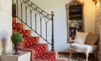 a red and gold staircase with ornate iron railings , leading to a white armchair and a black mirror at Hôtel Saint-Martin - la Maison Younan