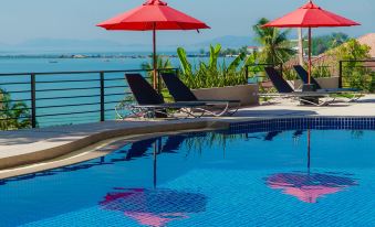 a beautiful swimming pool with red umbrellas and sun loungers , surrounded by lush greenery and a beautiful view of the sea at Play Phala Beach Rayong