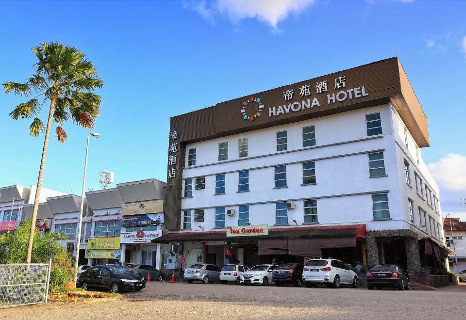 a city street with a large hotel on the side of the road , surrounded by cars and pedestrians at Havona Hotel - Kulai