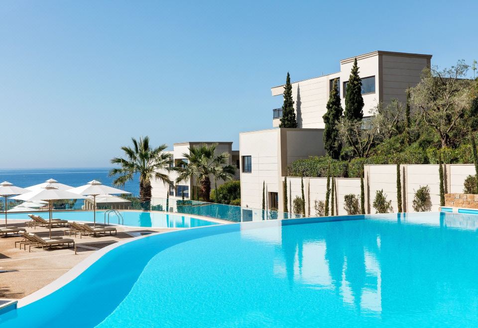 a large swimming pool with a building and palm trees in the background , under a clear blue sky at Ikos Oceania