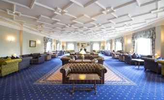 a large , open room with a blue carpet and rows of couches and chairs arranged for a gathering at Whittlebury Hall and Spa