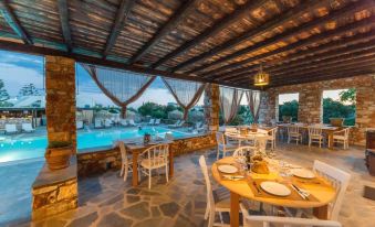 a dining room with a round table surrounded by white chairs , and a pool visible in the background at Parosland Hotel