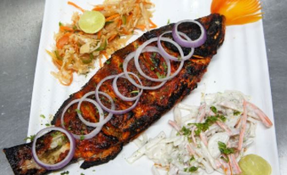 a large fish on a white plate , accompanied by a side of coleslaw and a wedge of lime at The Loft Hotel, Siliguri