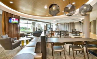 a modern dining area with wooden furniture , including tables and chairs , and a large window at SpringHill Suites Grand Forks