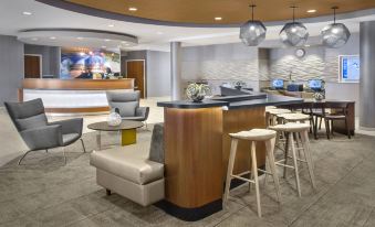 a modern hotel lobby with various seating options , including chairs and couches , as well as a bar area at SpringHill Suites Long Island Brookhaven