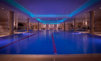a large indoor swimming pool with blue lighting , surrounded by wooden benches and steps , under the glow of ceiling lights at Lion Quays Resort
