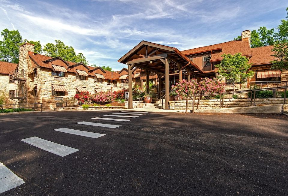 a large stone building with a wooden structure , surrounded by trees and flowers , under a blue sky with clouds at Cumberland Falls State Resort Park