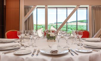 a large dining table is set with white plates , wine glasses , and silverware in front of a window overlooking a landscape at Exe Layos Golf