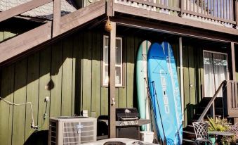 a green wooden house with a hot tub on the roof and two surfboards on the deck at Alpine Village Resort
