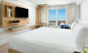 a modern hotel room with a large window offering a view of the ocean , a white bed , and a blue armchair at Allegria Hotel