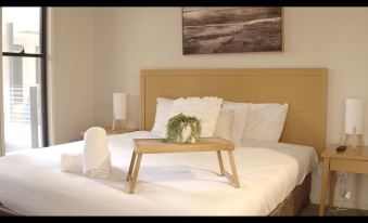 a bed with a wooden tray placed on it , along with a chair and a painting above the headboard at Barwon Heads Resort