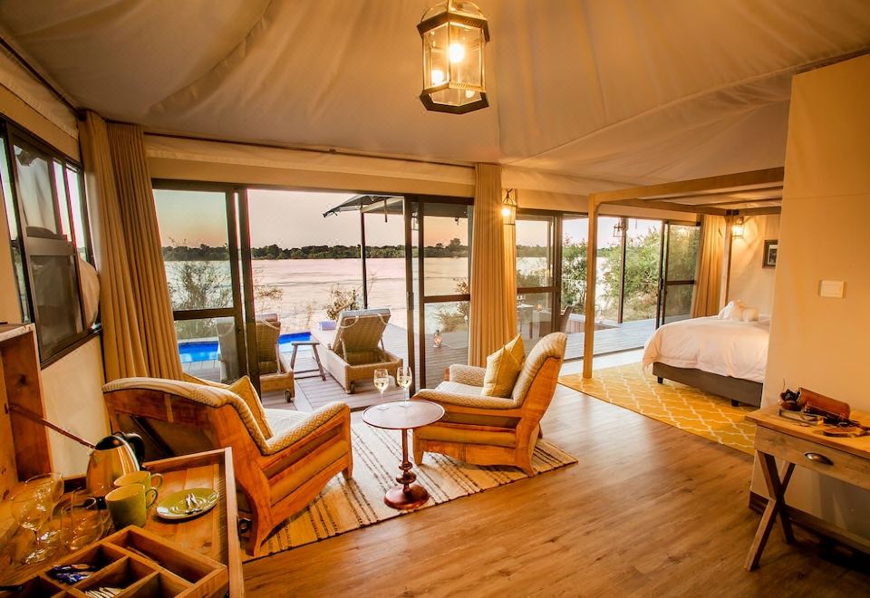 a spacious living room with a wooden floor and furniture , including chairs and a couch , overlooking a body of water at Old Drift Lodge