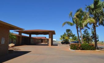 a large building with a covered entrance and a car parked in the driveway , surrounded by palm trees at The Lodge Motel