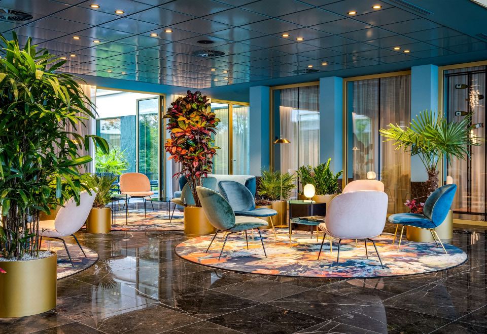 a modern lounge area with blue walls , white furniture , and a round rug , decorated with potted plants and flowers at NH Collection Antwerp Centre