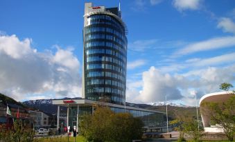 a tall , modern building with a glass facade is surrounded by trees and other buildings at Scandic Narvik