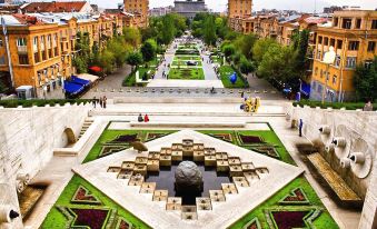 a grand garden with a large stone formation in the center is surrounded by colorful flowers and people walking around at Richmind Hotel