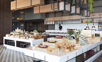 The restaurant features an open kitchen where food is displayed on the counter, and customers can dine at tables and chairs at Avani Sukhumvit Bangkok Hotel