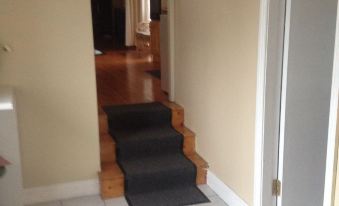 a hallway with a wooden floor and black carpeted stairs leading to an open doorway at Brigadoon