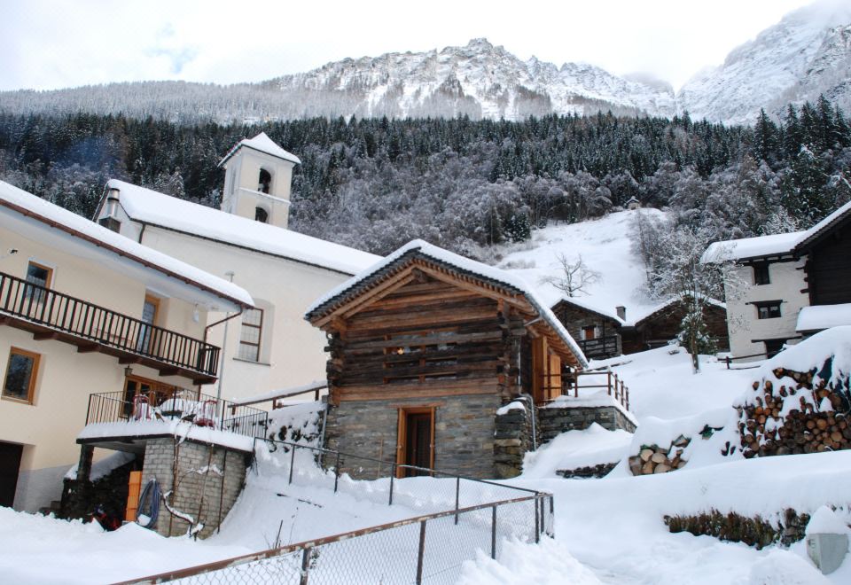 a snow - covered village with a small wooden building , surrounded by snow - covered mountains and a church at Melograno