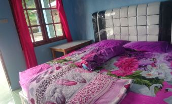 a bed with a purple and pink floral comforter is in a room with blue walls at Penginapan Rindu Alam Soala Gogo