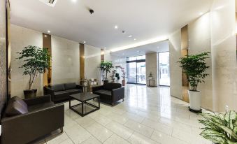 a spacious , well - lit lobby with white marble floors and walls , featuring black sofas and potted plants at The Empress Hotel