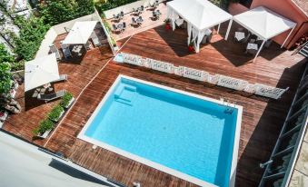 a large swimming pool is surrounded by a wooden deck and white umbrellas , with several lounge chairs and umbrellas nearby at Hotel Concorde