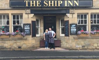 a man and a woman are standing in front of a hotel entrance , posing for a picture at The Ship Inn