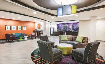 a well - lit lobby with various seating options , including couches and chairs , as well as a piano in the background at La Quinta Inn & Suites by Wyndham Houston Humble Atascocita
