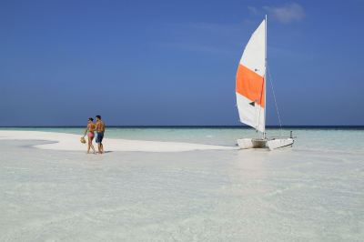 a couple is walking on a white sandy beach next to a sailboat in the ocean at Vilamendhoo Island Resort & Spa