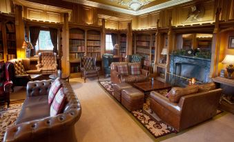 a spacious living room with brown leather couches , a fireplace , and a large bookshelf filled with books at Dalhousie Castle Hotel