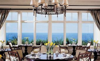 a dining room with a table set for a meal , surrounded by windows overlooking the ocean at Montage Laguna Beach