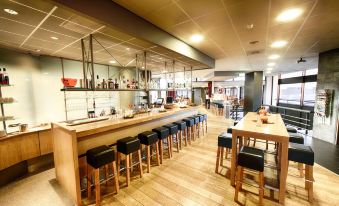 a modern restaurant with a long wooden bar and several black leather bar stools surrounding it at Leonardo Hotel Lelystad City Center