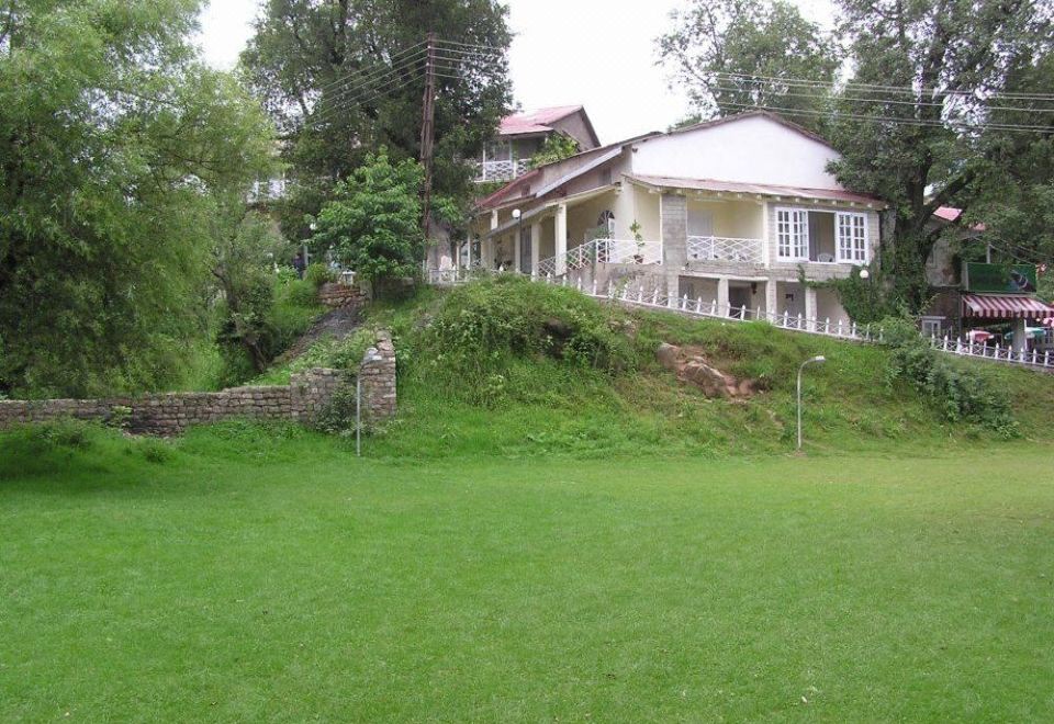 a large white house surrounded by a lush green lawn , with a soccer field in the background at Lockwood Hotel Murree