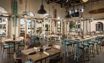 a modern restaurant with wooden tables , blue chairs , and hanging lights , creating an inviting atmosphere at Hyatt Regency Huntington Beach Resort and Spa