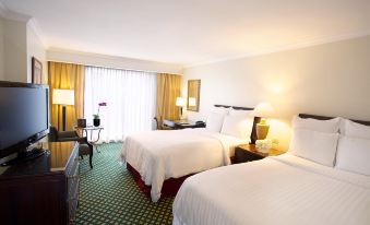 a hotel room with two beds , each made up with white sheets and pillows , standing next to a window with curtains at JW Marriott Hotel Caracas