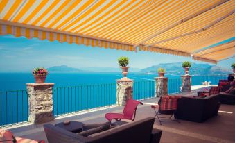 a patio with a colorful striped awning and several potted plants , overlooking the ocean at Hotel Caesar Augustus