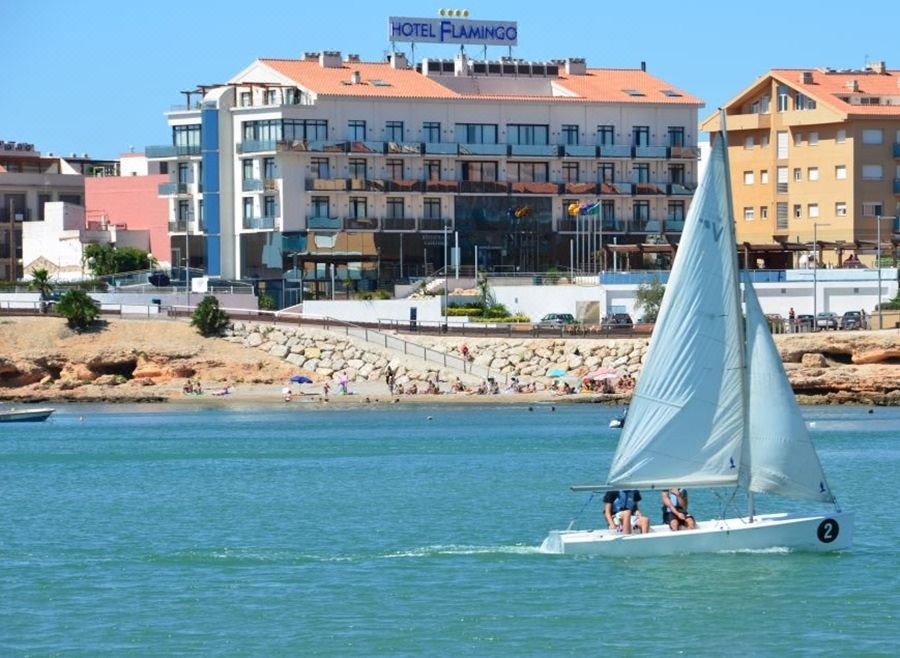 a sailboat with a flag on the side is sailing in front of a hotel at Hotel Flamingo