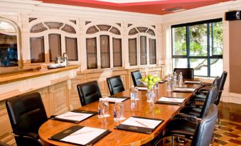 a conference room with a wooden table , chairs , and various items such as bottles , pens , and papers at The Prince of Wales Hotel