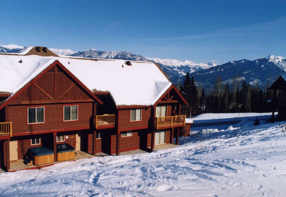a large wooden cabin with a red roof is surrounded by snow - covered mountains and trees at Whispering Pines