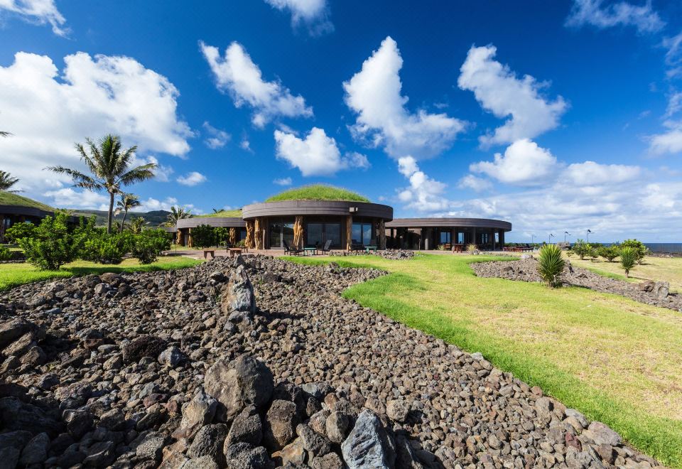 a large house surrounded by a grassy field and rocks , with a palm tree in the background at Nayara Hangaroa