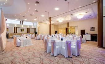 a large , well - lit banquet hall with white tables and chairs set up for a formal event at Hotel Boss