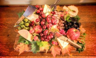 a wooden cutting board filled with various types of cheese , grapes , and other fruits , accompanied by a knife at Blueberry Hill Inn
