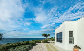 a white building on a sandy beach with a view of the ocean in the background at Saltwater - Absolute Oceanfront, Hot Tubs, Sauna, Fire Pits