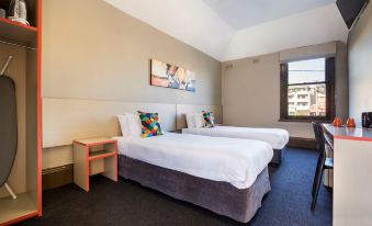 a hotel room with two beds , a nightstand , and a window , decorated with white bedding and colorful pillows at Granville Hotel