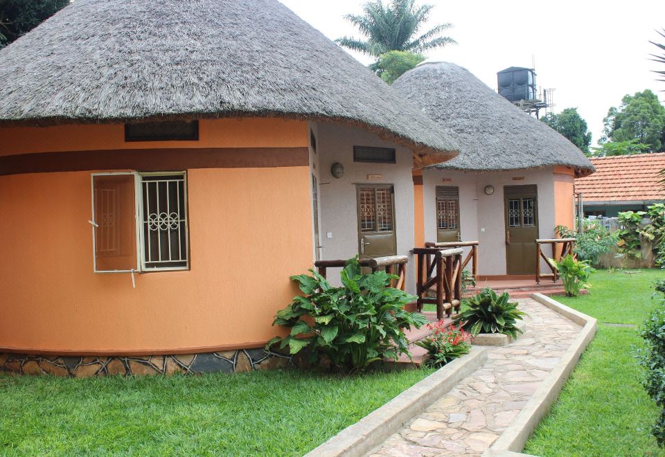 a small , orange - colored house with thatched roofs and green plants in front of it , under a cloudy sky at Lake Victoria View Guesthouse