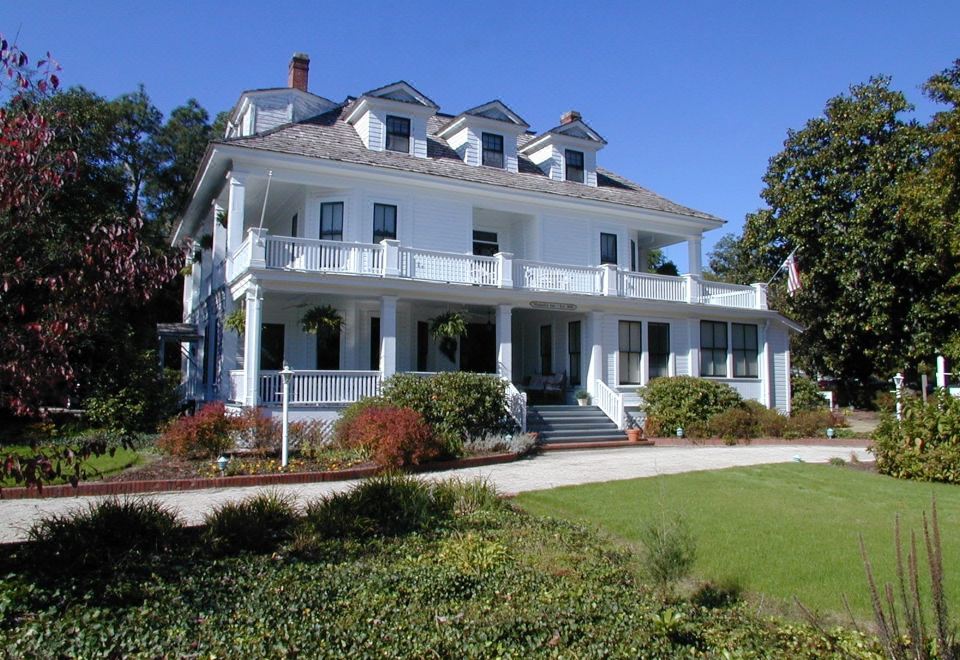a large white house with multiple balconies and columns , situated in a lush green field at Magnolia Inn
