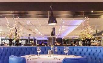 a dining room with blue booths and chairs , a table set for two , and pendant lights hanging above at Hello Hotel