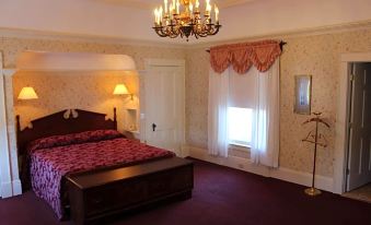 a well - lit bedroom with a bed , nightstands , and curtains , as well as a chandelier hanging from the ceiling at White Inn