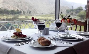 a table is set with plates of food , wine glasses , and silverware in front of a window overlooking a mountainous landscape at Guizado Portillo Hacienda & Resort