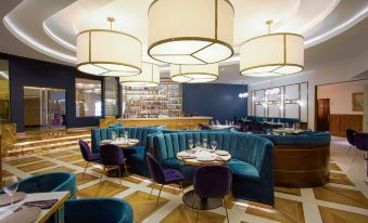 a modern restaurant with blue and white furniture , including couches , chairs , and tables , as well as pendant lights hanging from the ceiling at Grand Hotel Tijuana